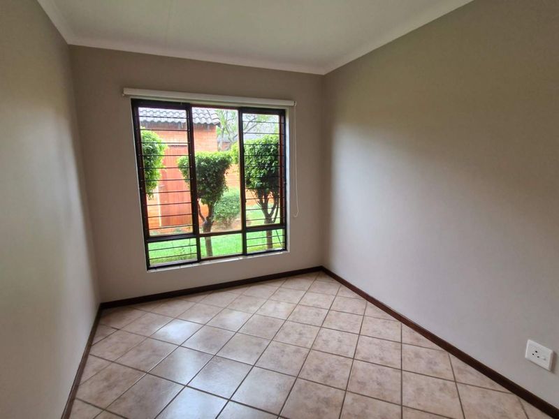 A clean, empty bedroom featuring neutral wall paint, tiled flooring, and a window fitted with security bars.