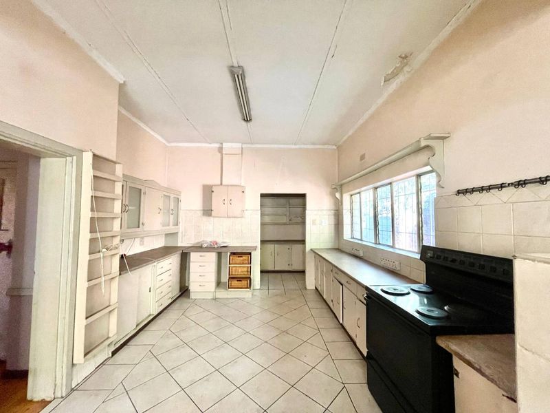A dated kitchen featuring extensive built-in cabinetry, tiled flooring, and a tiled splashback, requiring cosmetic updates and ceiling repairs.