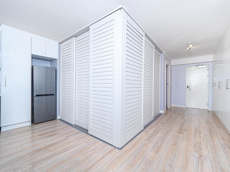 A clean and modern entry area featuring light wood-look laminate flooring, extensive built-in storage with shutter-style doors, and a secure main entrance.