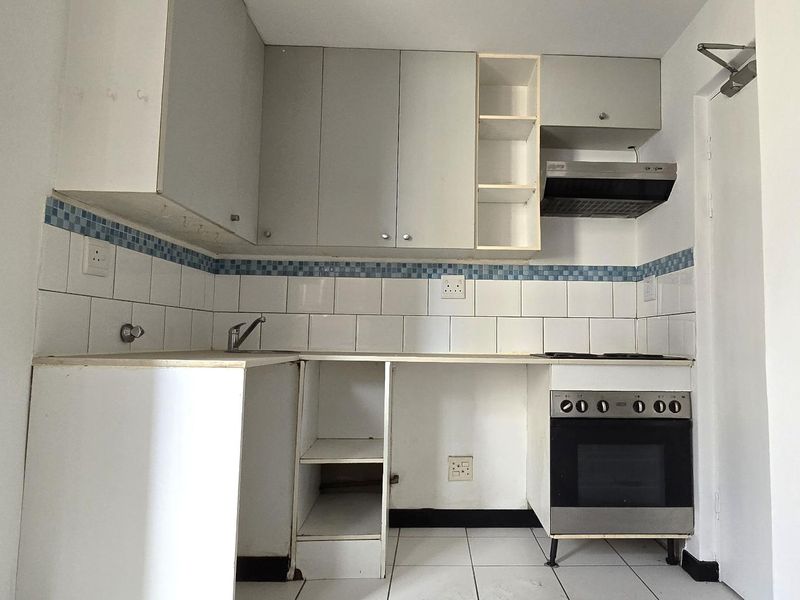 A compact kitchen featuring built-in cabinetry, a tiled backsplash, and integrated oven and hob, currently vacant and ready for updates.
