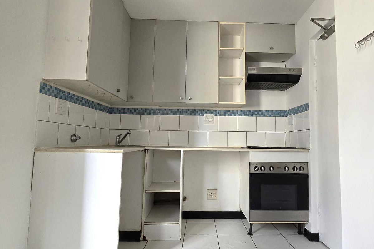 A compact kitchen featuring built-in cabinetry, a tiled backsplash, and integrated oven and hob, currently vacant and ready for updates.