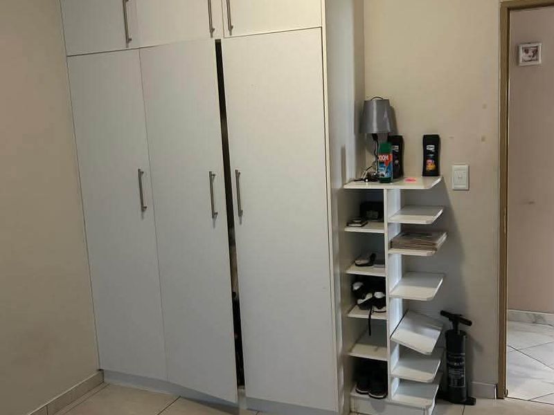 A bedroom featuring white built-in cupboards with modern handles and neutral tiled flooring, offering practical storage space.