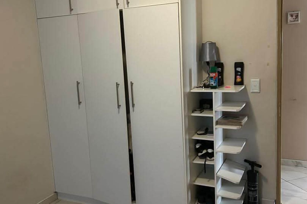 A bedroom featuring white built-in cupboards with modern handles and neutral tiled flooring, offering practical storage space.