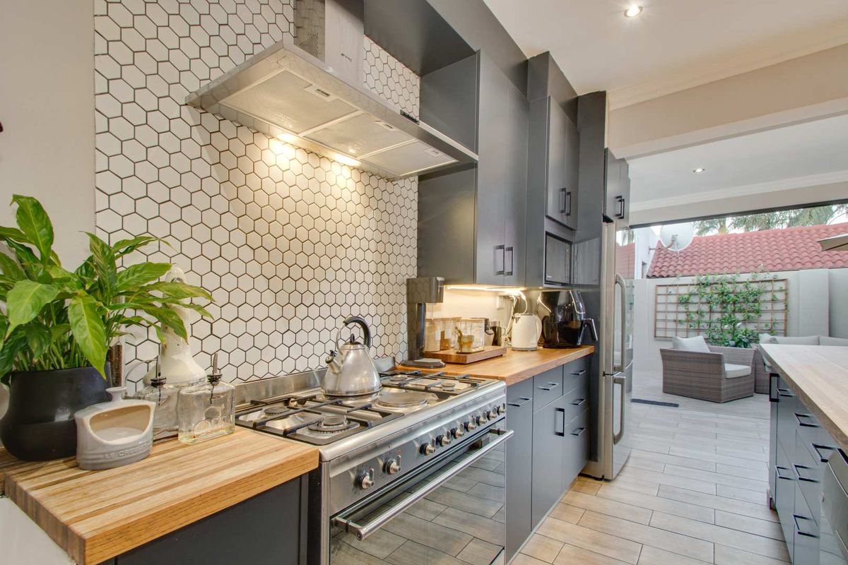 Modern kitchen featuring dark cabinetry, wooden countertops, a gas stove with extractor fan, and a stylish hexagonal tile backsplash.