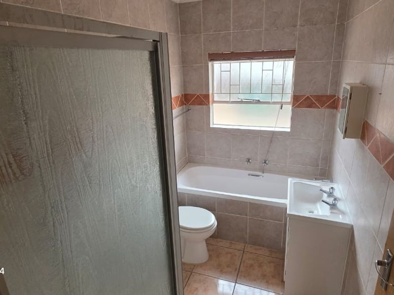 A functional bathroom featuring a shower enclosure, bathtub, toilet, and vanity basin with neutral wall and floor tiling.
