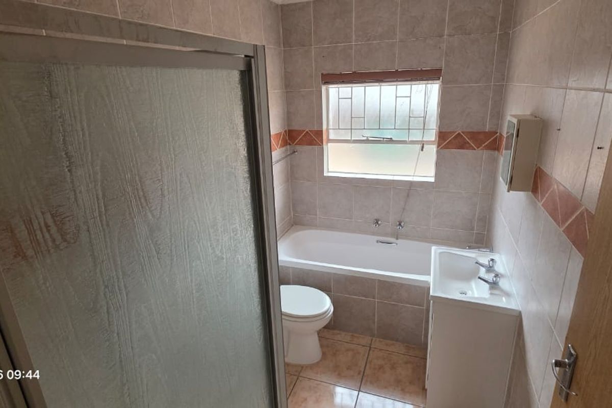 A functional bathroom featuring a shower enclosure, bathtub, toilet, and vanity basin with neutral wall and floor tiling.