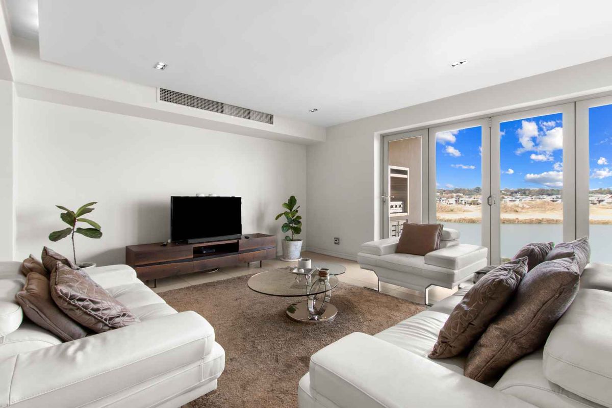 Spacious living room featuring recessed ceiling lighting, ducted air conditioning, and large glass doors opening to a balcony with scenic water views.