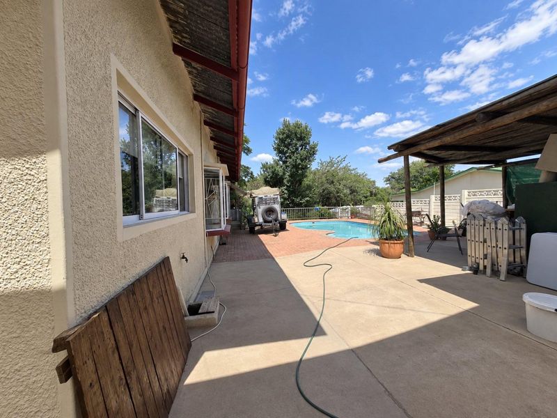 Outdoor entertainment area featuring a swimming pool, concrete patio, and a covered pergola structure with brick paving.