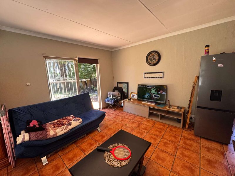 A living room featuring tiled flooring and a sliding glass door with security gate, providing access to the exterior.