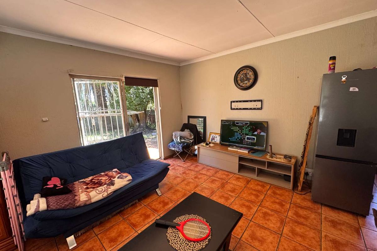 A living room featuring tiled flooring and a sliding glass door with security gate, providing access to the exterior.