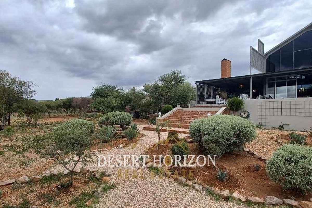 Rear view of the property featuring a landscaped garden, gravel pathway, brick staircase, and a covered patio area with large glass windows.