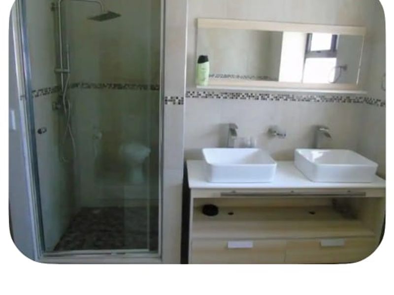 Modern ensuite bathroom featuring a double vanity with vessel sinks, wall-mounted faucets, and a glass-enclosed shower with a rain shower head.