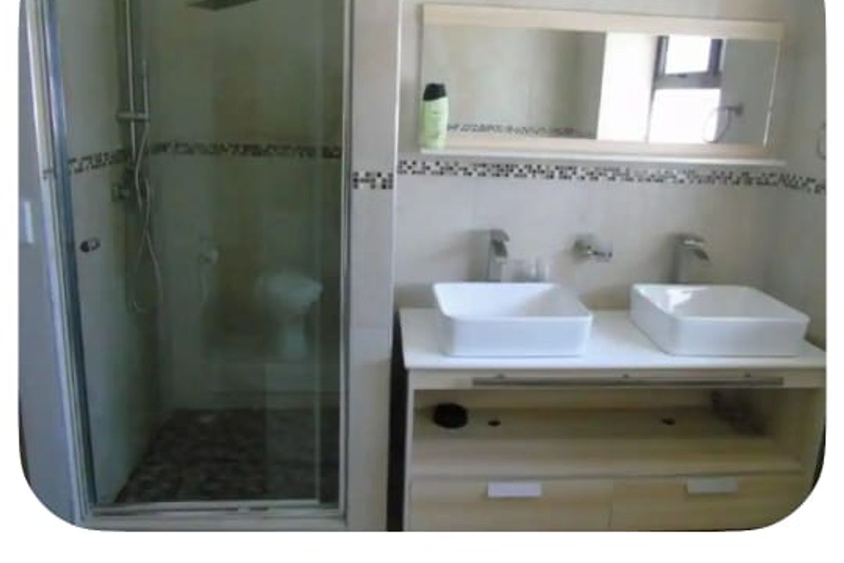 Modern ensuite bathroom featuring a double vanity with vessel sinks, wall-mounted faucets, and a glass-enclosed shower with a rain shower head.