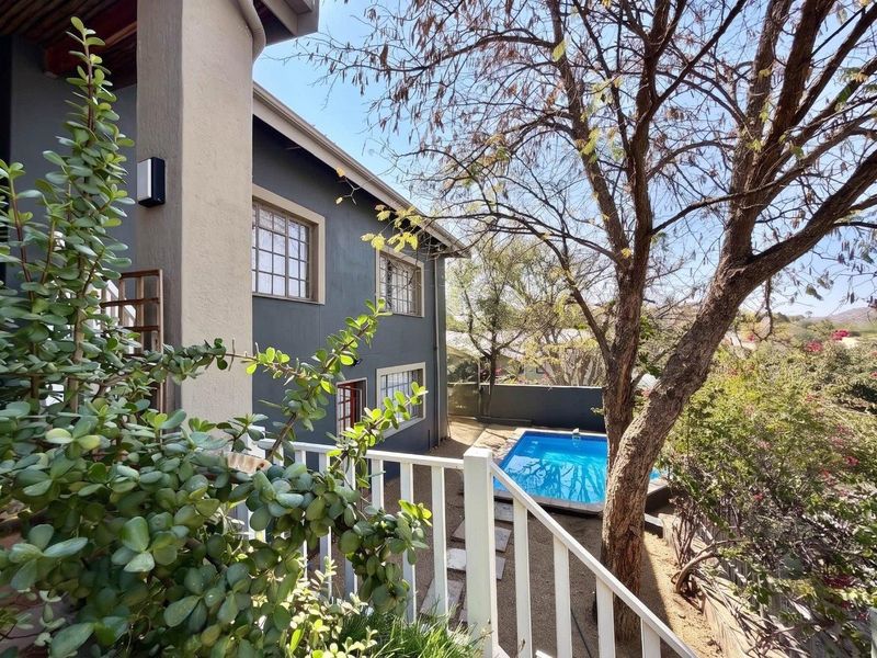 Rear view of the property featuring a swimming pool, landscaped garden area, and a balcony with white railings overlooking the backyard.