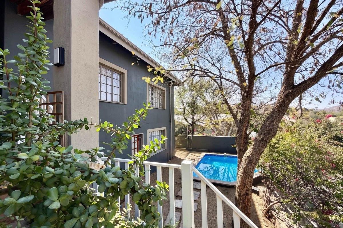 Rear view of the property featuring a swimming pool, landscaped garden area, and a balcony with white railings overlooking the backyard.