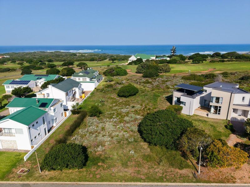 Aerial view of a vacant residential plot situated in a coastal estate, surrounded by established homes and natural vegetation with ocean views.