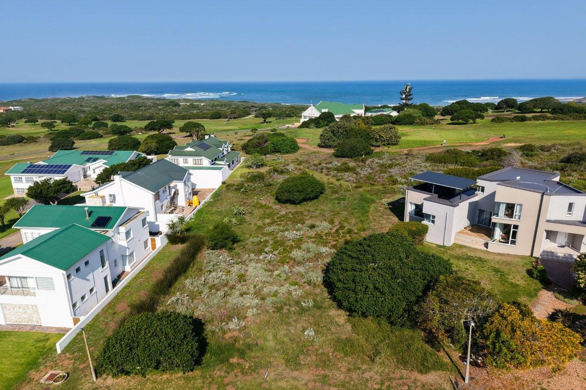 Aerial view of a vacant residential plot situated in a coastal estate, surrounded by established homes and natural vegetation with ocean views.