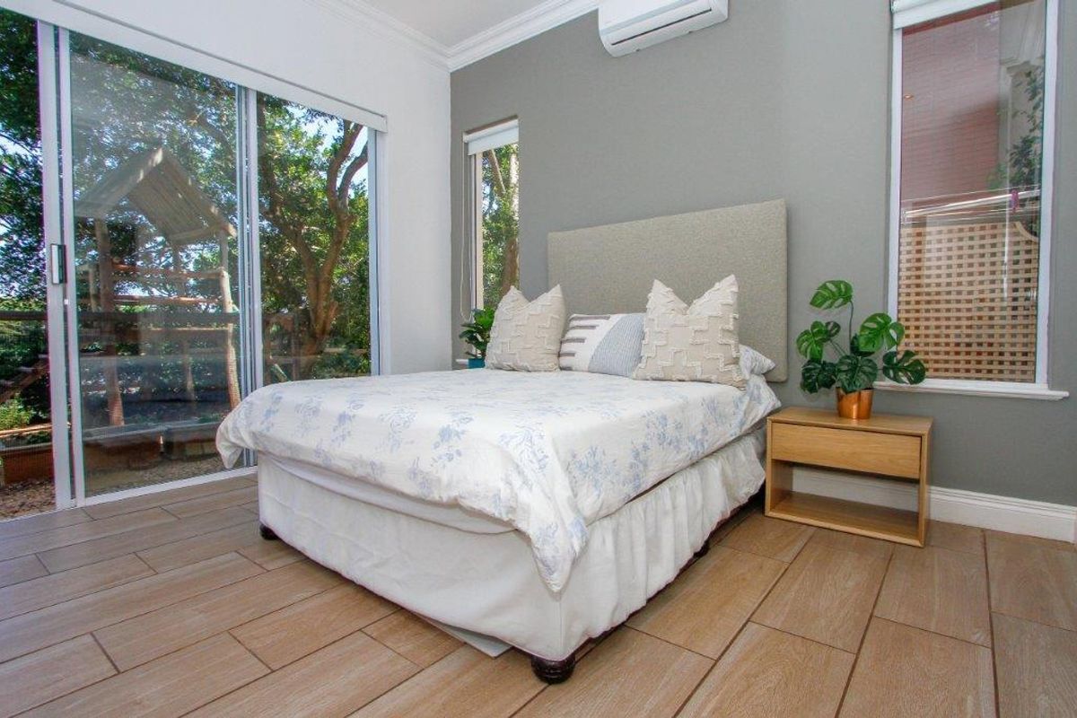 A well-maintained bedroom featuring tiled flooring, a split-system air conditioner, and large sliding glass doors providing natural light and garden views.