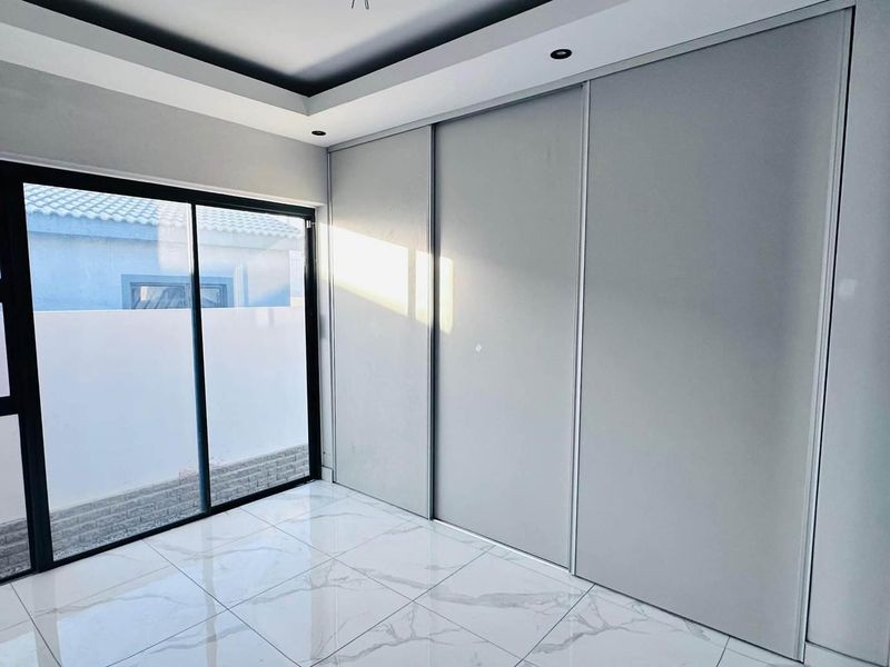 Modern bedroom featuring large built-in sliding wardrobes, polished marble-look tile flooring, recessed tray ceiling lighting, and a sliding glass door leading outdoors.
