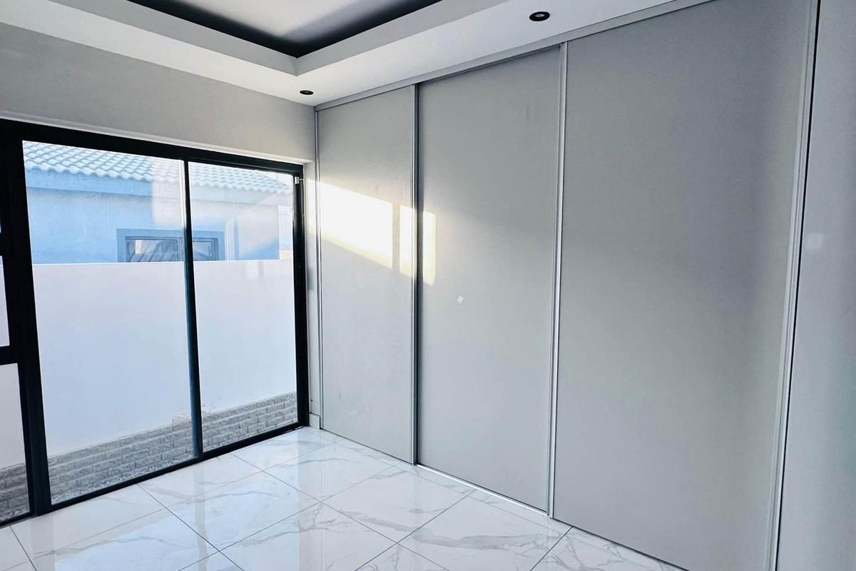 Modern bedroom featuring large built-in sliding wardrobes, polished marble-look tile flooring, recessed tray ceiling lighting, and a sliding glass door leading outdoors.