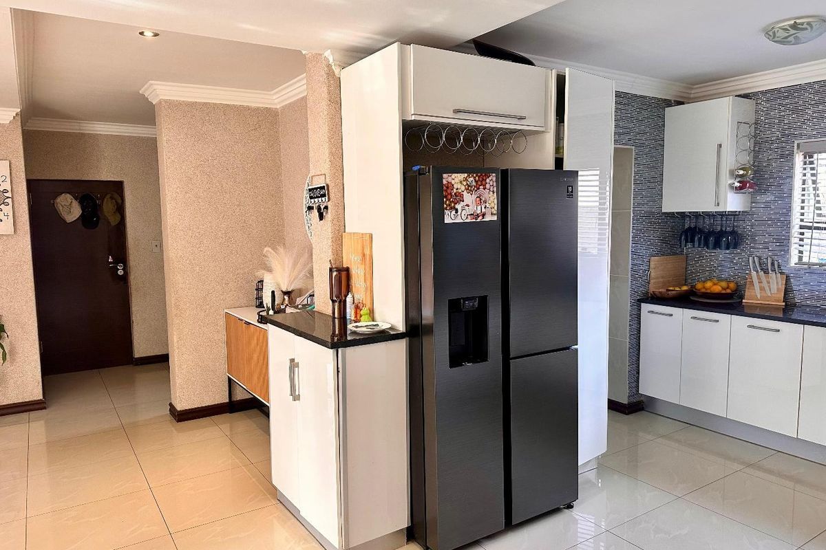 Modern kitchen featuring white cabinetry, dark countertops, tiled splashback, and polished floor tiles, seamlessly integrated into an open-plan living space.