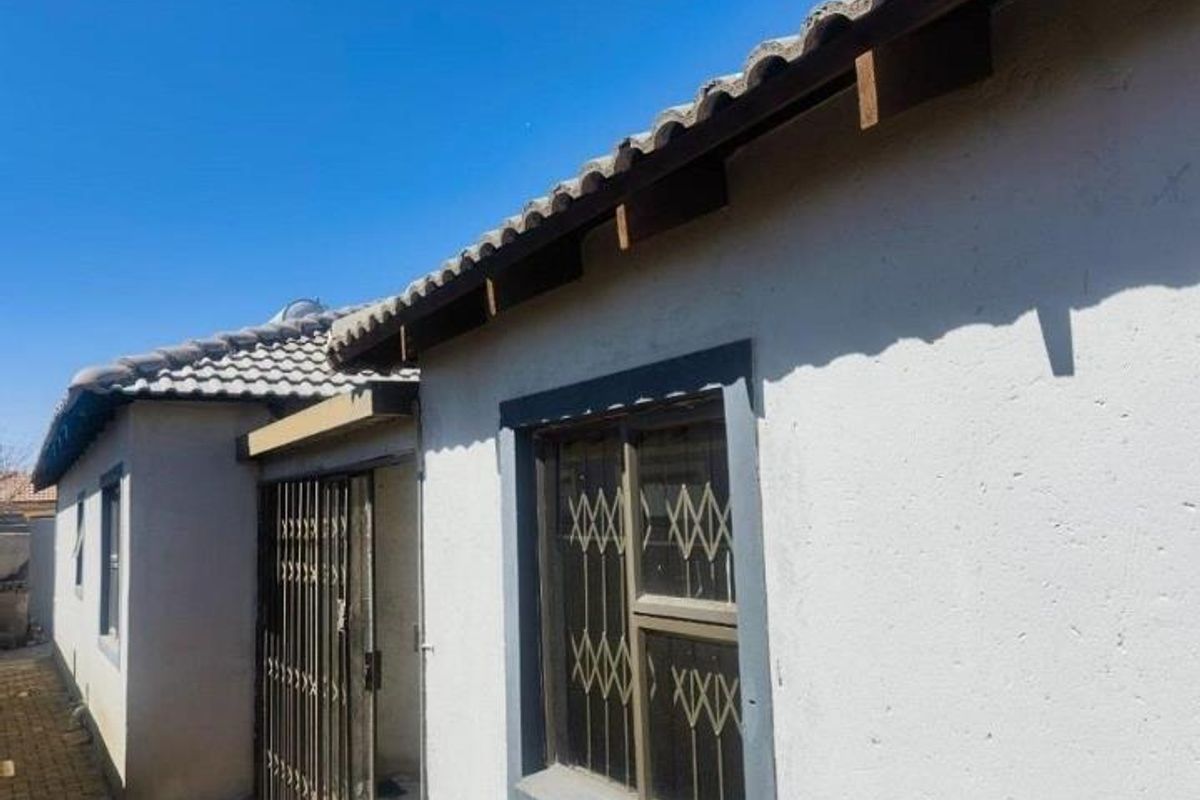 Exterior view of the property showing a tiled roof, security gates, and window bars on a plastered facade.