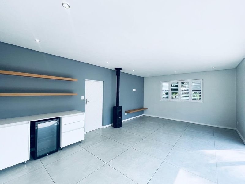 Spacious living area featuring modern tiled flooring, a sleek freestanding fireplace, built-in cabinetry, and floating shelves, illuminated by recessed downlights.