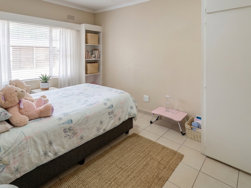 A bedroom featuring tiled flooring, a built-in wardrobe, and integrated shelving, providing a functional and neutral living space.