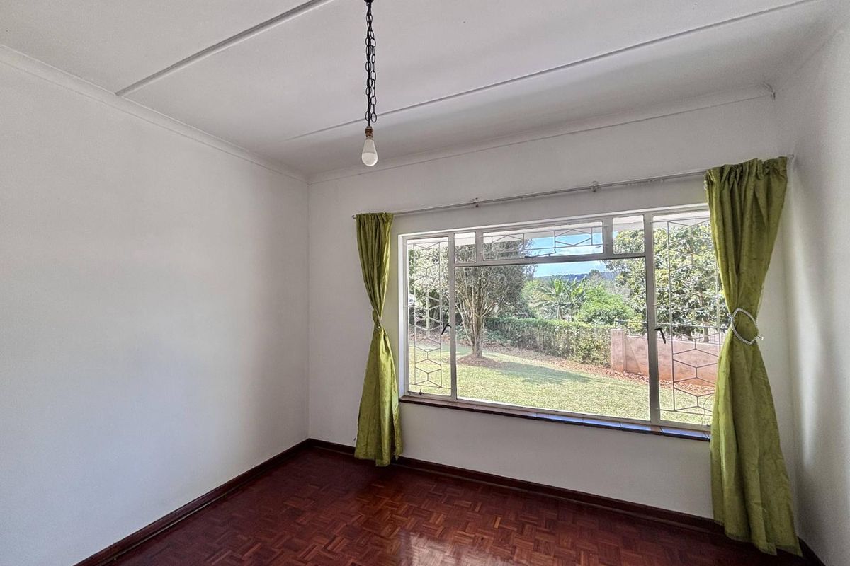 A bright, empty bedroom featuring classic parquet flooring, a large window with security bars, and a simple pendant light fixture.