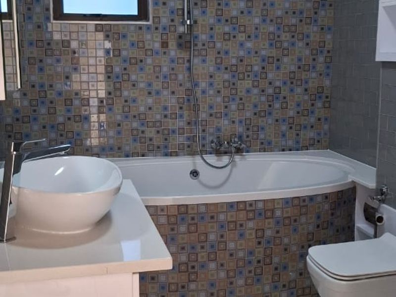 Modern bathroom featuring a built-in bathtub with mosaic tile surround, wall-hung toilet, vessel sink on a vanity, and large format floor tiles.
