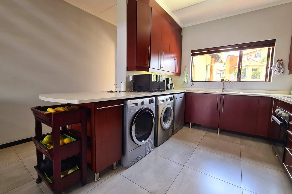 A functional kitchen featuring dark wood cabinetry, light countertops, tiled flooring, and integrated laundry appliances, offering a practical layout for daily use.