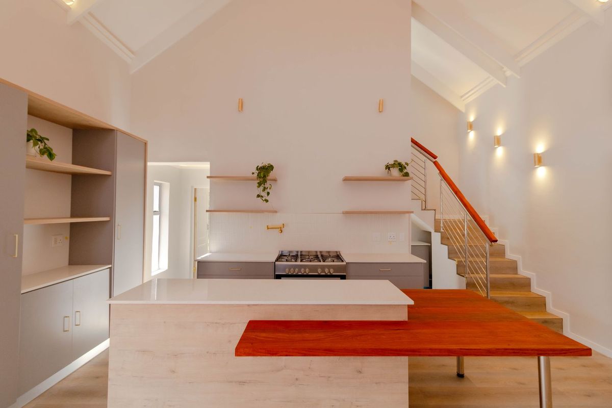 Modern open-plan kitchen featuring a gas hob, stone countertops, floating shelving, and a striking timber-accented island, set beneath a high vaulted ceiling.