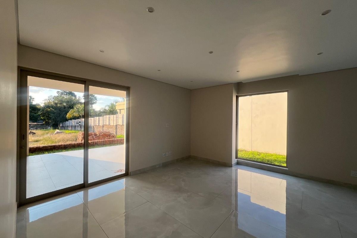 A bright, empty living room featuring large sliding glass doors, polished tile flooring, and recessed ceiling lighting.
