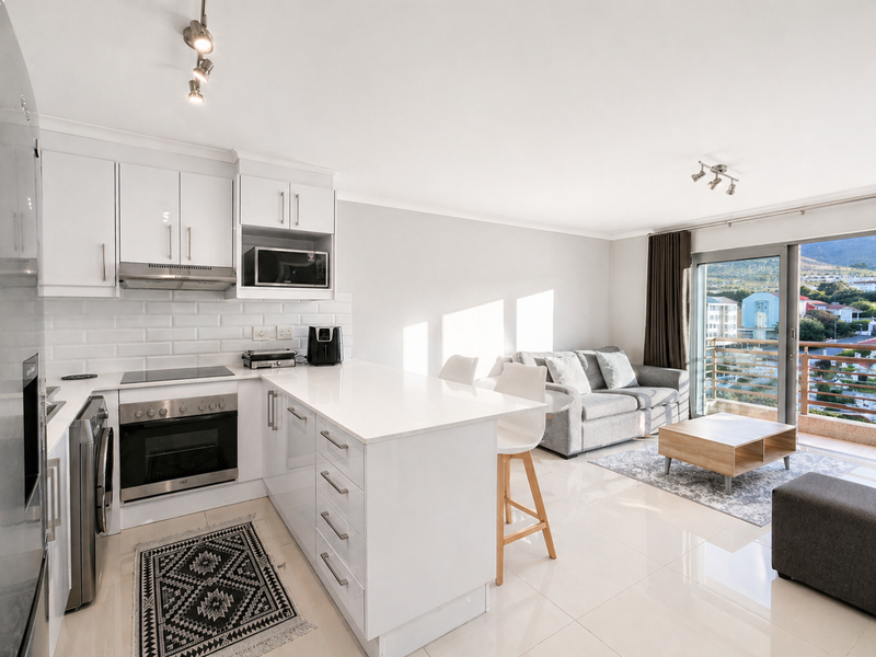 Modern open-plan kitchen and living area featuring sleek white cabinetry, stone countertops, subway tile backsplash, and direct access to a balcony with scenic views.