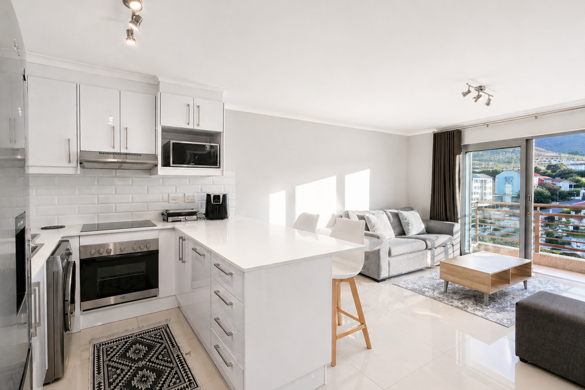 Modern open-plan kitchen and living area featuring sleek white cabinetry, stone countertops, subway tile backsplash, and direct access to a balcony with scenic views.