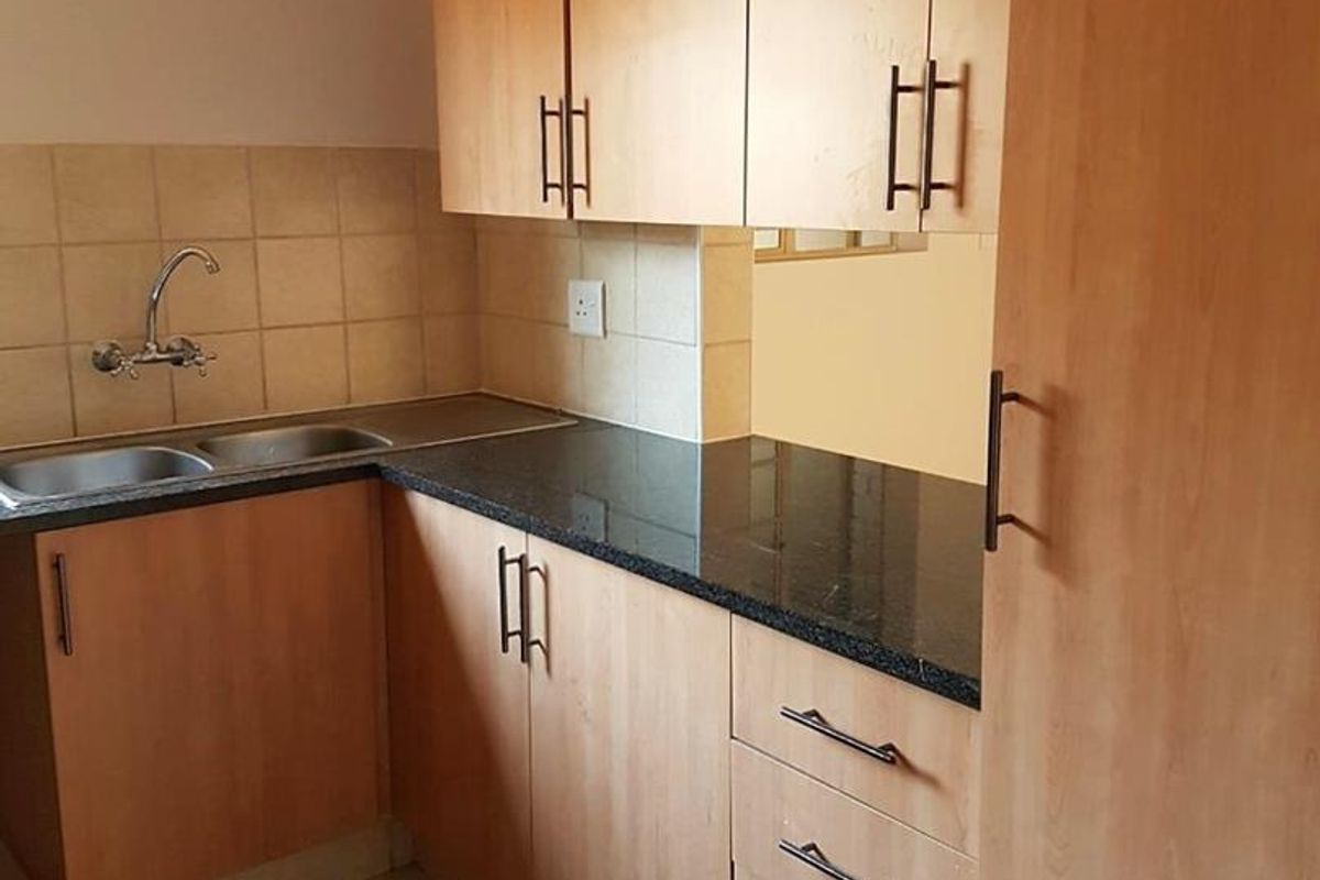 A functional kitchen featuring laminate cabinetry, granite countertops, a double bowl stainless steel sink, and tiled flooring.