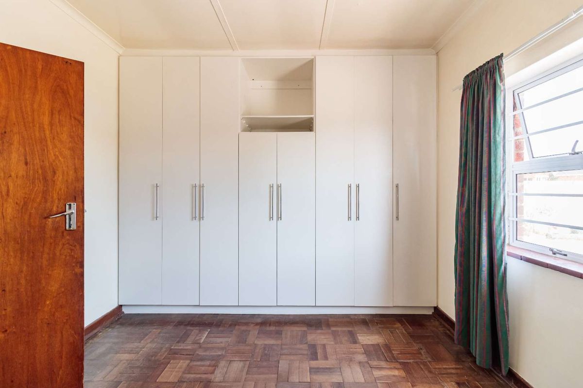A bright, empty bedroom featuring classic parquet flooring, ample built-in cupboard storage, and a window with natural light.