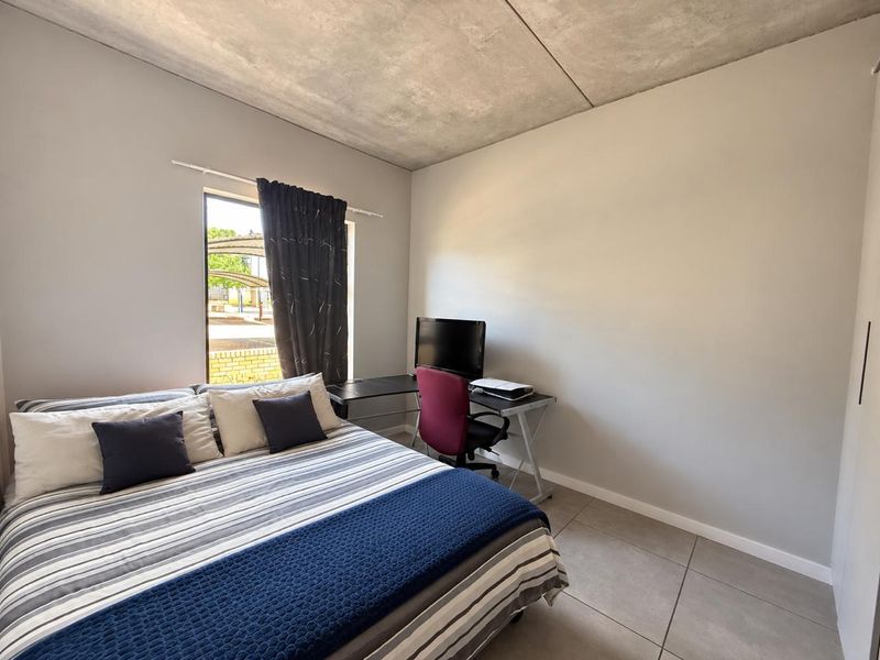 A modern bedroom featuring an exposed concrete ceiling, large format floor tiles, and a built-in wardrobe, offering a clean and contemporary living space.