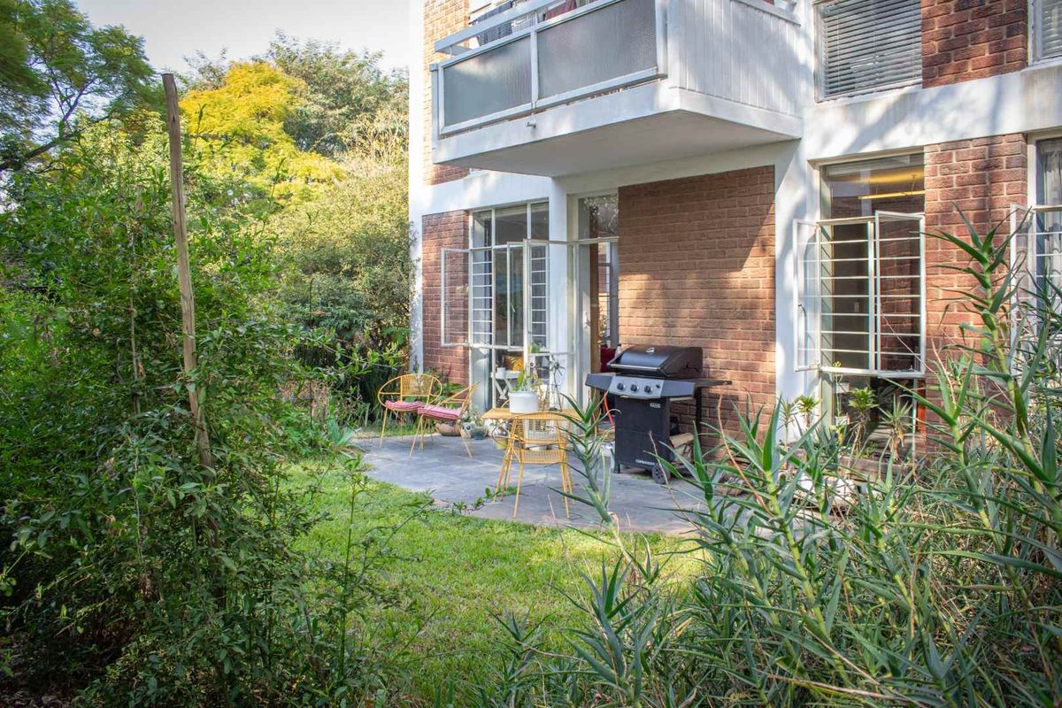 Rear view of the apartment building featuring a paved patio area, small lawn, and a balcony above.