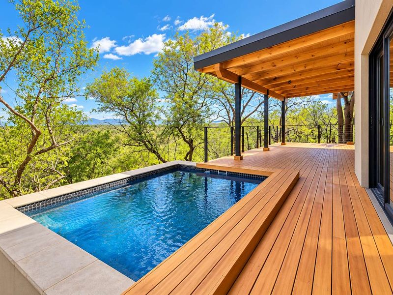 A modern outdoor living space featuring a plunge pool, expansive timber decking, and a covered patio area overlooking a natural bushveld landscape.