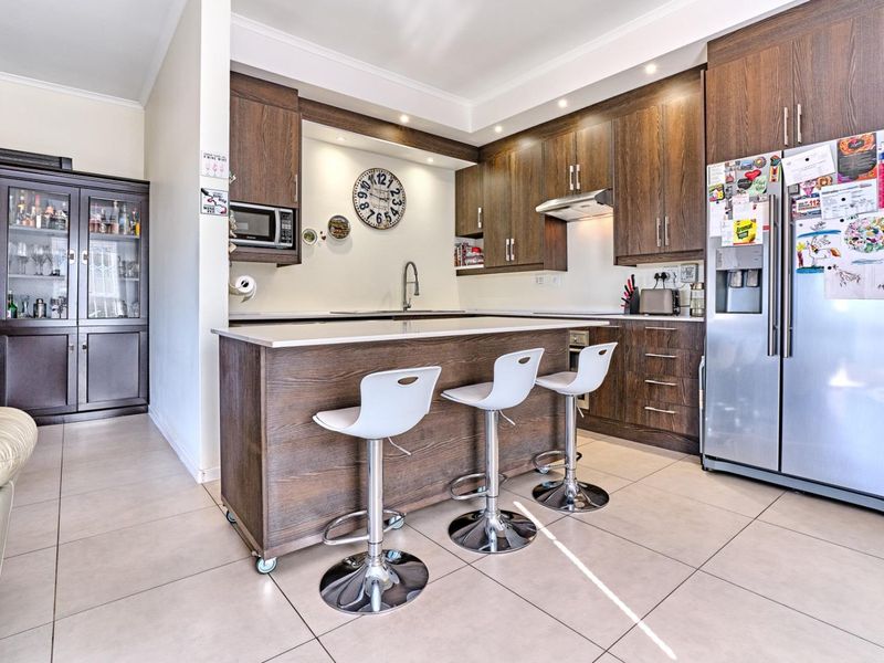 Modern kitchen featuring dark wood cabinetry, a central island with breakfast bar seating, stone countertops, and integrated appliances.
