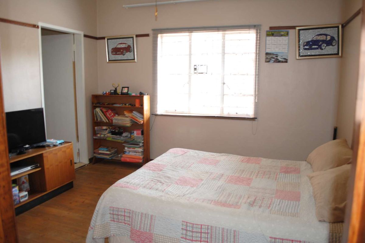 A functional bedroom featuring timber flooring, a large window with security bars, and picture rails.