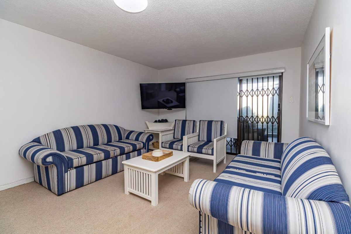 A living room featuring neutral carpeting and a sliding glass door with a security gate leading to an outdoor area.