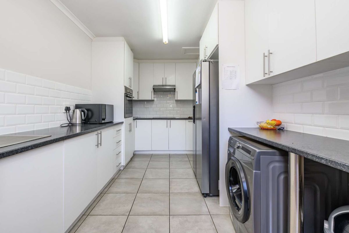 A functional kitchen featuring white cabinetry, dark laminate countertops, subway tile backsplash, and tiled flooring with integrated appliance spaces.