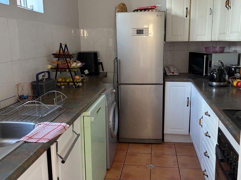 A functional kitchen featuring white cabinetry, laminate countertops, tiled backsplash, and integrated appliances, offering a practical layout for daily meal preparation.