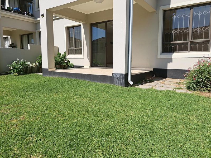 Rear view of the apartment featuring a covered patio with tiled flooring, sliding door access, and a private garden area.