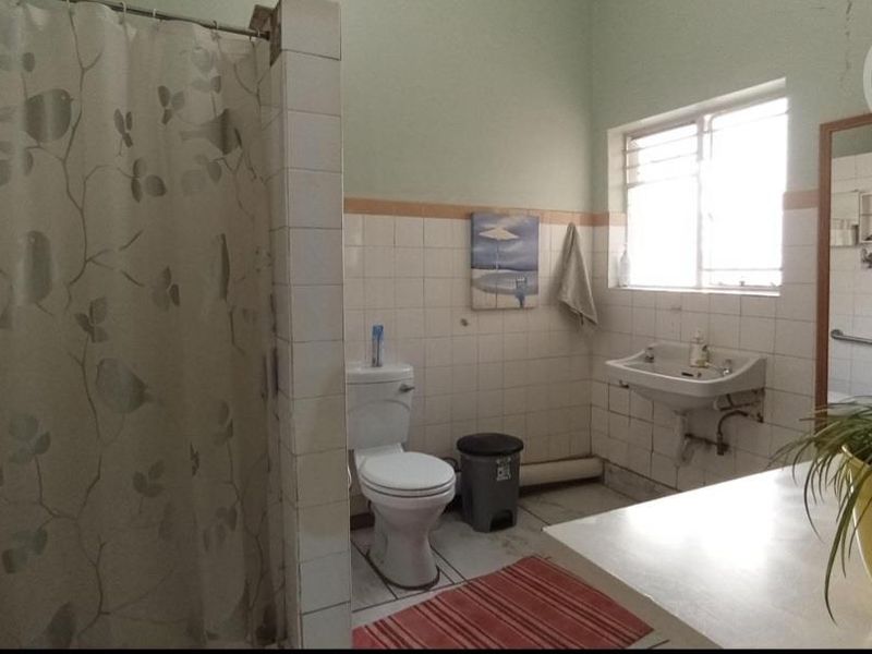 A functional bathroom featuring a shower enclosure, wall-mounted basin, and toilet, with dated ceramic tiling and visible plumbing fixtures.