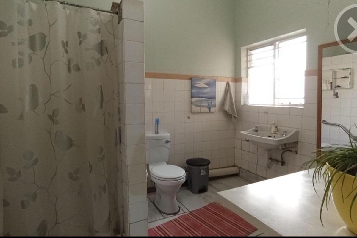 A functional bathroom featuring a shower enclosure, wall-mounted basin, and toilet, with dated ceramic tiling and visible plumbing fixtures.