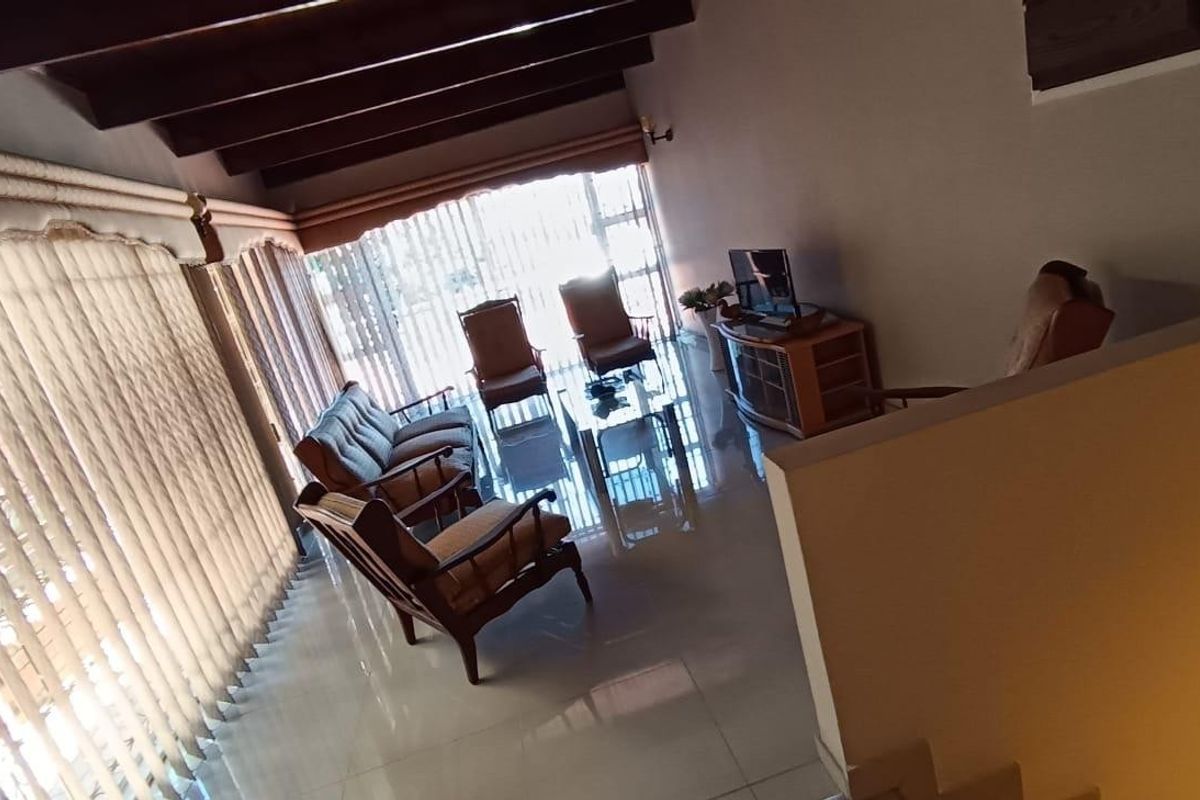 Spacious living room featuring exposed timber ceiling beams, polished tiled flooring, and large sliding glass doors providing ample natural light.