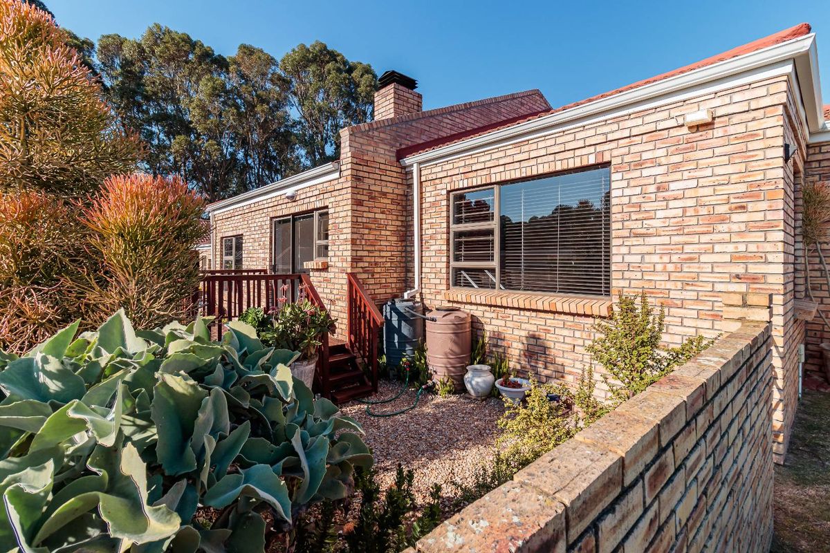 Rear exterior view of a brick house featuring a raised timber deck, brick chimney, and rainwater collection tanks.